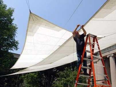 Gary Cunha of Facilities tightens cables that hold up the sail, which protects faculty, administrators and guests from sun and rain at Commencement.