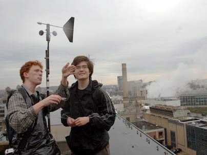Fourth-year Ph.D. student in materials science Dan Wesolowski, left, discusses wind direction and velocity on a rooftop with mechanical engineering sophomore Richard Bates. They and other students put equipment on a number of roofs around the Institute for a month to determine the viability of using wind turbines to generate power. MIT's co-generation plant is visible behind them.