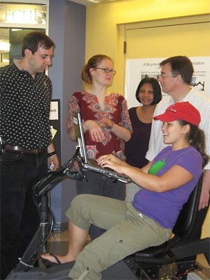 MIT student Julia Kiberd '08 pedals the specially adapted exercise bike, generating power for the laptop she's using to check her e-mail. Helping to host the Student Center display of the bike are (from left) technical instructor Stephen Rudolph, Kendra Johnson '09, IT energy coordinator Laxmi Rao and civil and environmental engineering senior research associate John Germaine.