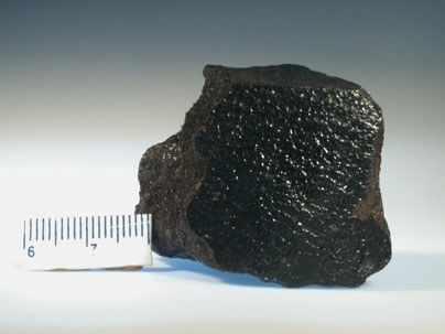 A picture of the first discovered (and therefore eponymous) angrite "Angra dos Reis"; which was observed to fall from the sky in 1869 near the town of Angra dos Reis in Brazil.Â  The black; shiny face was produced from melting of the meteorite's surface during passage through Earth's atmosphere.Â  Scale bar is in centimeters.