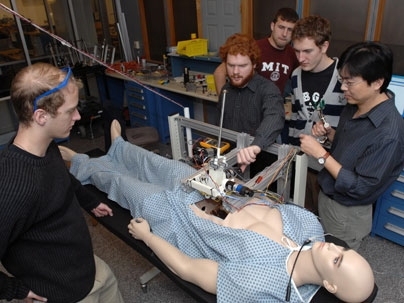 Senior Paul Blascovich watches surgical robot operating from left, while teaching assistant Lael Odhner plays with arm. Junior Tony McDonald watches from back, Junior Ian Rust and instructor Harrison Chin watch from center and right of "patient."