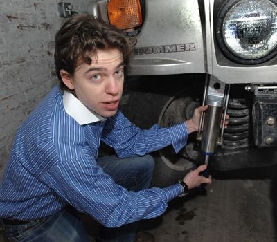Zack Anderson, senior in elecrical engineering and computer sciences, holds a GenShock prototype up to a Humvee coil spring where it is installed.