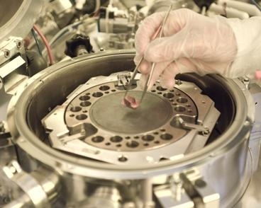 Graduate student Will Chung displays a hybrid chip being developed in Professor Tomas Palacios' lab. The machine in the background is used to combine the semiconductor materials into one chip.