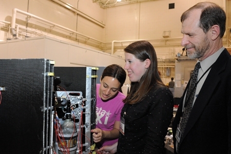 John Keesee looks on as the seniors Frances Gonzalez and Emily Grosse complete the installation of solar panel restraints on the satellite before they begin x-axis vibration tests.