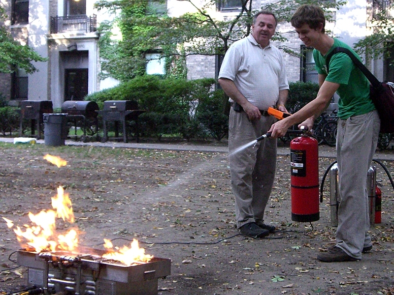 Mark Collins (left), the Emergency Coordinator and Life Safety Officer at Harvard University, shows a student the proper way to extinguish a fire. The technique is called PASS: Pull the pin; Aim at the base of the fire; Squeeze the lever slowly; Sweep from side to side. The test fire was produced by a BullEx box, which has sensors to determine where the trainee is aiming and to vary the flames in ...