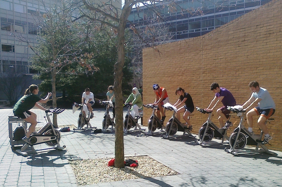 Lauren Hanley, assistant director of fitness for DAPER, left, takes advantage of the warmer weather and takes her group cycling class outside of the Wang Fitness Center.
