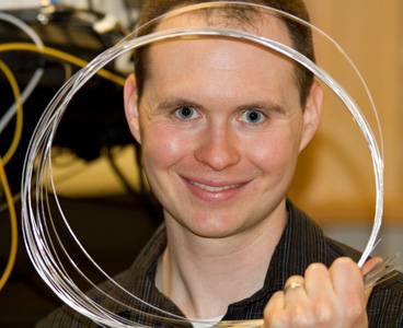 Nicholas Orf, a postdoctoral researcher at MIT who was lead author of a paper describing the synthesis of materials inside a fiber. He is holding samples of fibers produced in the lab.