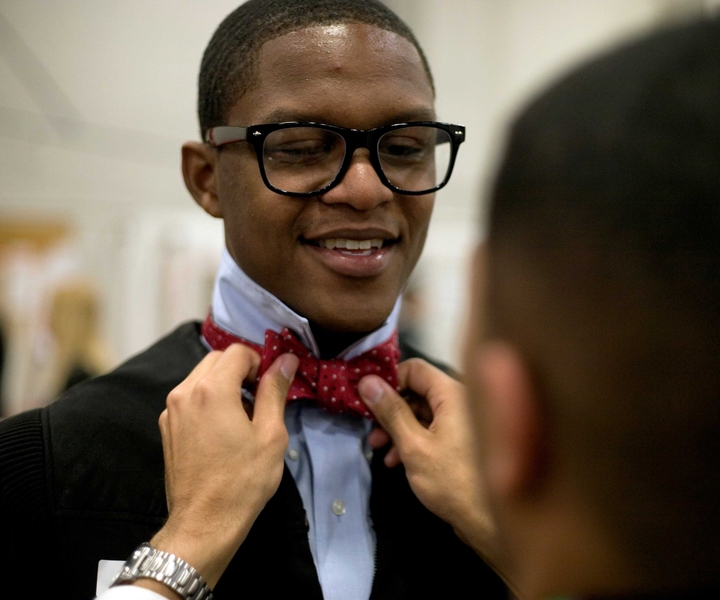 A student has his bowtie adjusted as he gets ready and dons his regalia.