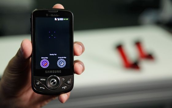 The results screen on the smartphone showing maps for position and size of the cataract, on screen left, and density of each section, on screen right. At top is the pattern of five colored dots that is fed into the clip-on device (removed in this picture) to perform the actual cataract test.