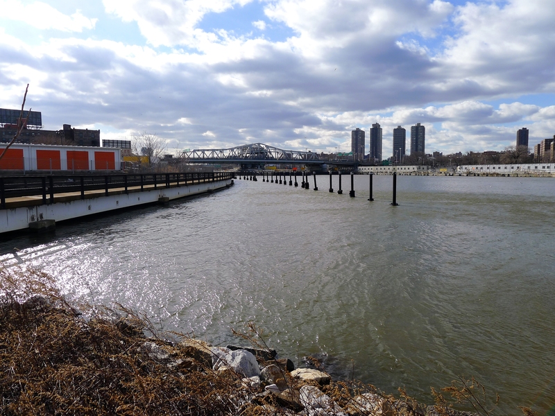 A Bronx-side view of the waterfront's existing conditions, featuring natural edge conditions, elements of the industrial working waterfront, the freight railroad, storage facilities, and the 3rd Avenue Bridge spanning the Harlem River.