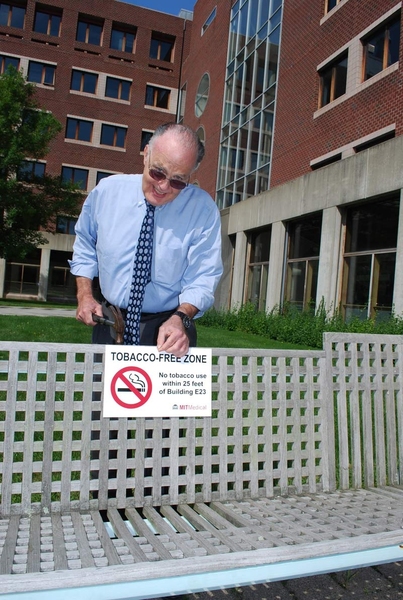 Dr. William Kettyle, medical director of MIT Medical, 'installs' one of the new signs that will be placed around Building E23, signifying the new tobacco-free zone within 25 feet of MIT Medical.