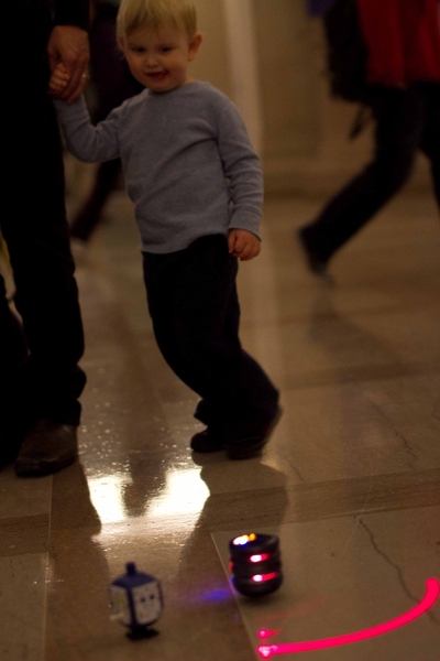 Two-year-old Liam Parisky-Kern holds the hand of his father, Senior Leadership Giving Officer Brian Kern, while he keenly observes a light-up, singing dreidel at the lighting of MIT Hillel’s test tube menorah on Tuesday.
