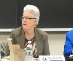 Gina McCarthy sits at a table in front of a blackboard
