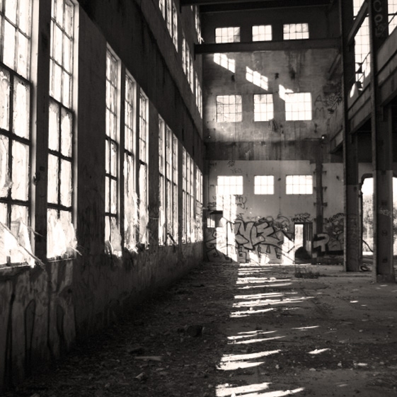 Nighttime black and white photo outside a warehouse where the lights are on, and the exterior wall has been marked with graffiti 