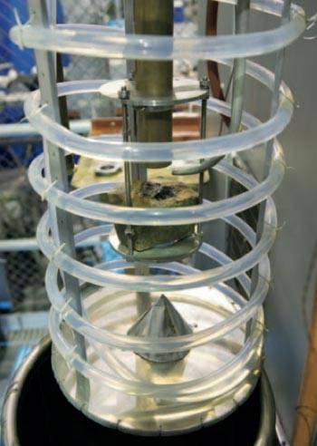 In this setup, a gyrotron at the top sends a continuous millimeter-wave beam through the copper tube toward the rock sample at the center, and water flows through the surrounding coil. During operation, the device is lowered into the steel chamber below and sealed. Based on the flow volume and temperature rise of the water, the researchers can deduce how much of the incoming energy is absorbed by ...