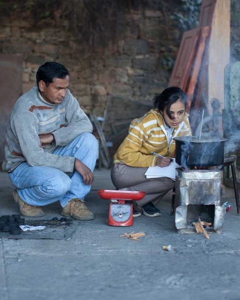 Viral Modi '13 measures how long it takes for charcoal made out of pine needle to heat two liters of water, to compare it to other charcoal as well as wood and LPG, in Avani, India. On the left, Chanchal, a community partner looks on.