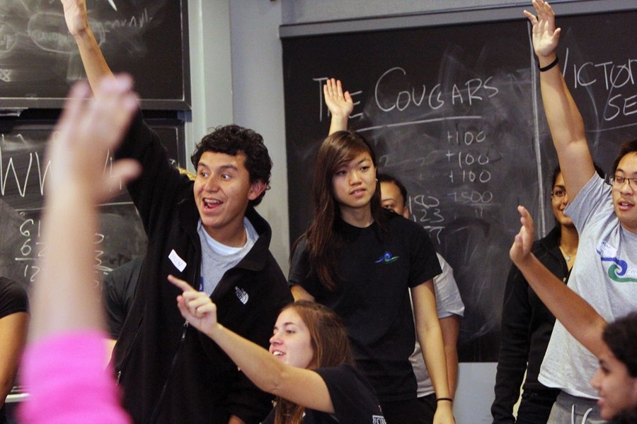 Achievers Andy Cortes, left, and Minh-Hieu Tran, right, raise their hands vigorously as they vie to answer the math Jeopardy! question of the day. Mentor Sarah Huang, middle, and Liz Bishop, bottom left, cheer on their Achievers.