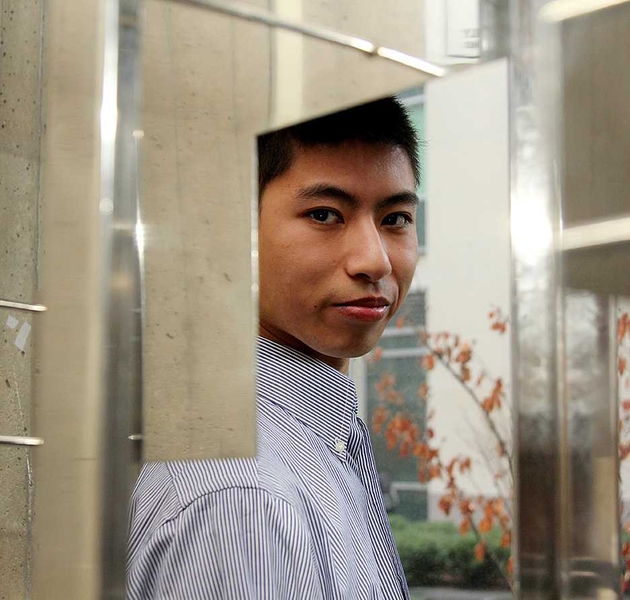 Eric Trac reflects through mirror on campus building wall.