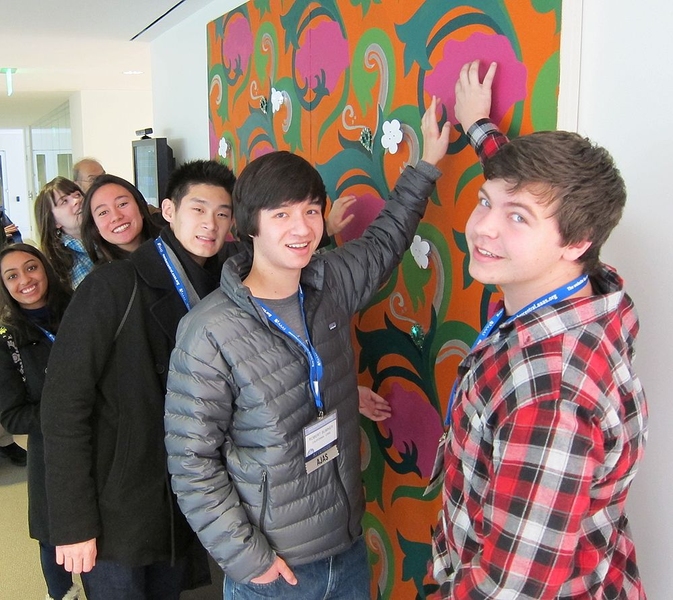 High school students gather around a tapestry designed by MIT Media Lab's High-Low Tech group. Touching certain parts of the tapestry causes its lights to turn on or off.