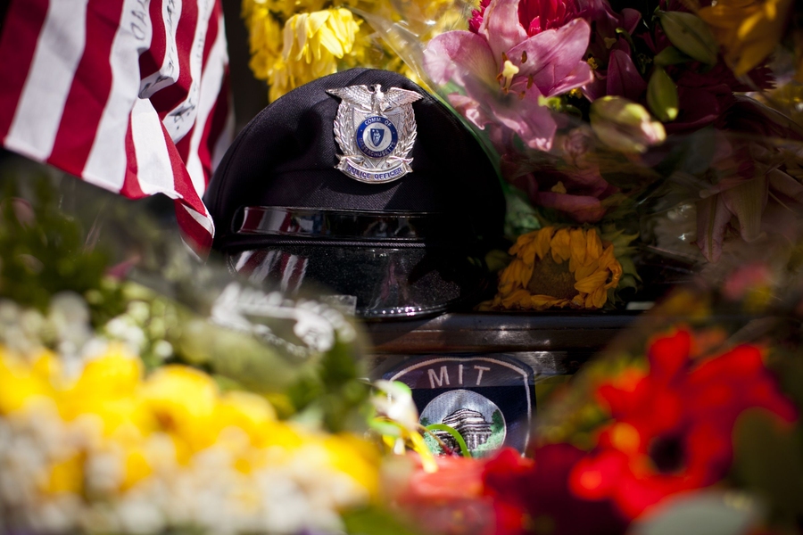 The memorial includes flowers, personal notes, flags and MIT Police regalia.