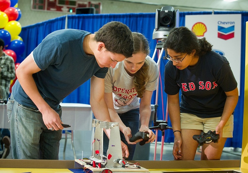 Preparing for a head-to-head competition between two robots, students and staff check out the operation of controllers used to operate one of the robots.