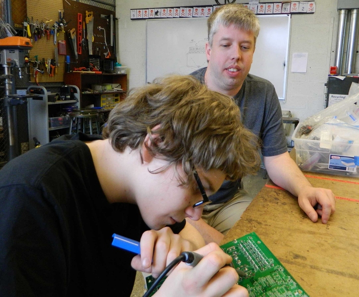 Daniel Sheen, a junior at the John D. O'Bryant School of Mathematics and Science, and frequent Saturday Thing participant, receives guidance from alumni volunteer Mike Allen while soldering a circuit board to be used for the musical laser harp.