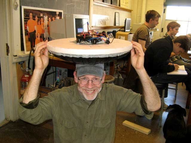 Edgerton Instructor Ed Moriarty holds a small battery-powered hovercraft above his head made by students in The Saturday Thing.