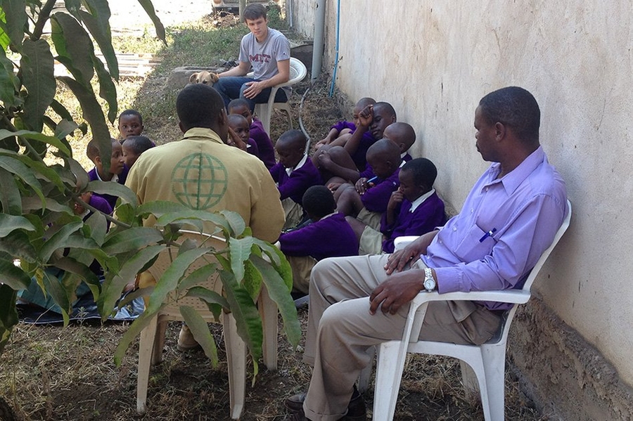 Tebes (background) gathers with Tanzanian schoolchildren, their teacher and Bernard Kiwia (back to camera) outside a workshop.