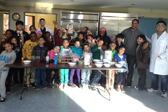 Suan Tuang stands with group of about 30 elementary school students in classroom.