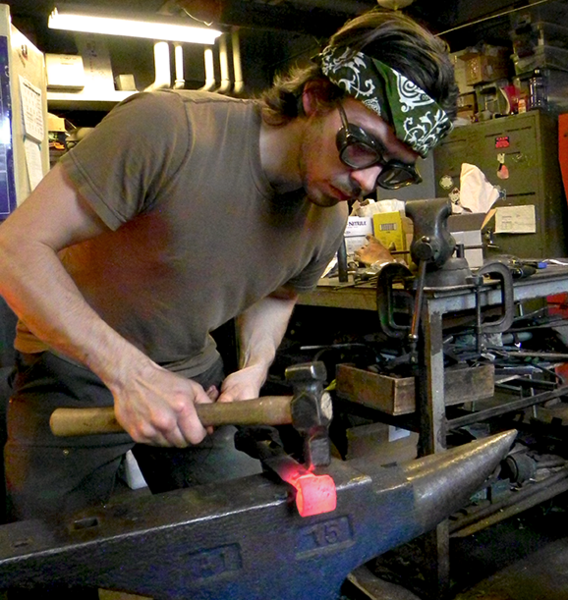 Hunter hammers a glowing the hot metal blade to shape an opening for the handle of the froe.
