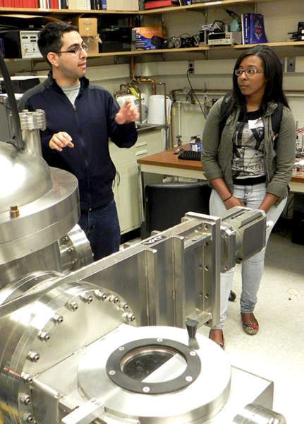 Graduate student Ahmed Al-Obeidi (left) explains a “sputter” deposition machine for creating thin films and battery material to Summer Scholar Kayla Robinson during a tour of MIT professor Carl Thompson’s Materials for Micro and Nano Systems lab.