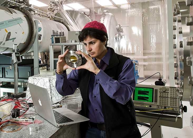 Nergis Mavalvala stands in a lab looking at a small electronic device