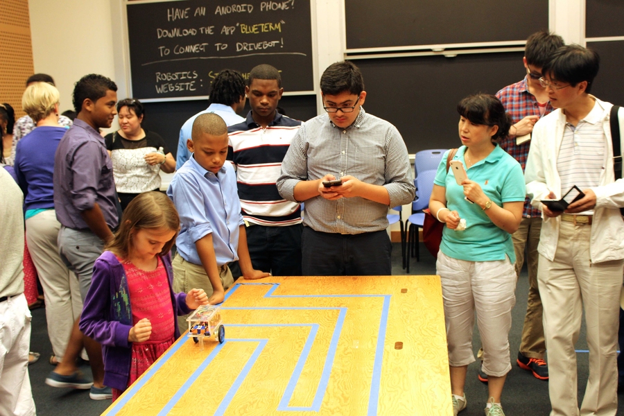 Level-four student Luis Franco (center) test drives his final robotics project at the 2014 STEM Sumer Institute Final Ceremony as level one student Kevin Matos (second from left) and other STEM Program family members look on.