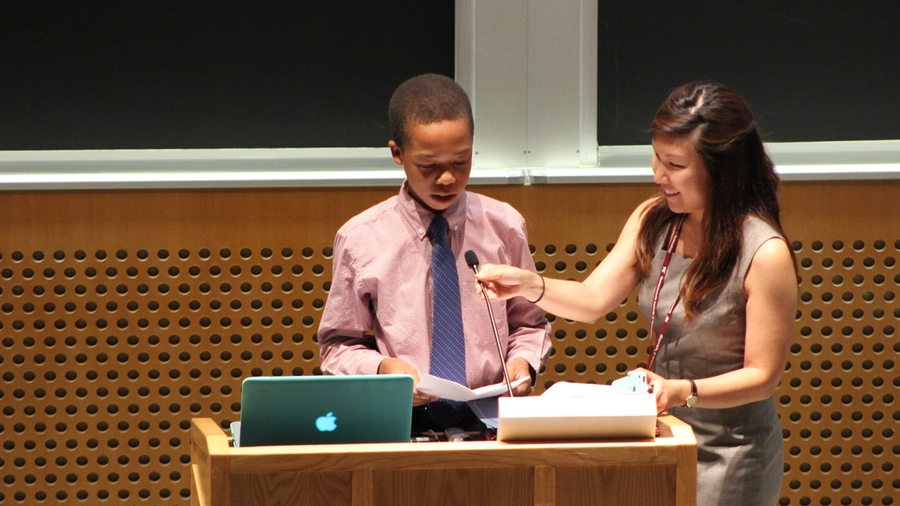 Lead Academic Advisor Catherine Park (right) introduces level-two student Rhocar Constant before his speech at the 2014 STEM Summer Institute Final Ceremony. Each level elected a student speaker to represent their class to tell family members and friends about their experience with the STEM Program this summer.