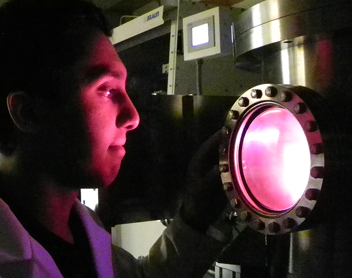 Rahul Kini peers into an electron sputtering machine used to create thin film batteries. The faint glow comes from plasma in the sputtering process. “What we’re really trying to achieve is high energy density, high energy capacity and reusability,” Kini says.