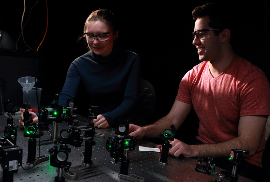 A. Jolene Mork, a fifth-year MIT graduate student in chemistry, and Mark C. Weidman, a fourth-year MIT chemical engineering graduate student, work with an array of mirrors and lenses coupled to a laser that directs a light beam to a microscope (not shown) for carrying out time-resolved photoluminescence spectroscopy experiments in the Tisdale Lab at MIT. 