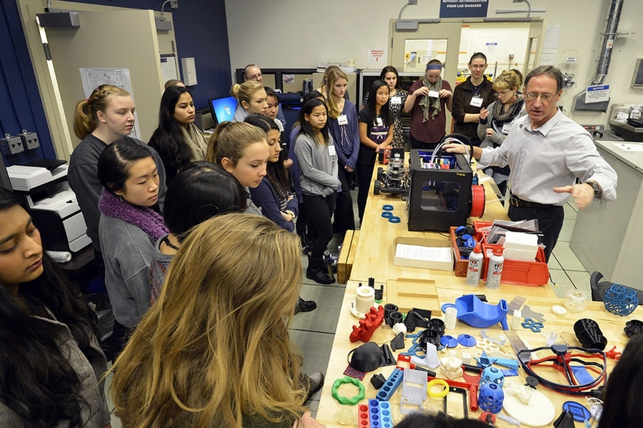 David Scott, manager of the Technology Office Innovation Laboratory, explains to the girls at the Lincoln Laboratory workshop how a MakerBot 3-D printer functions and what kind of parts it can make. On the bench, 3-D-printed parts of various shapes, sizes, and complexities are displayed.
