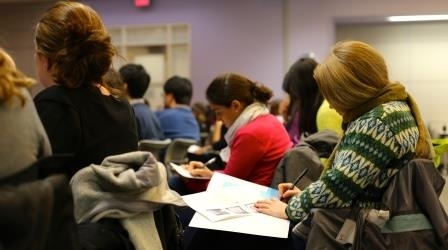 Half a dozen people sit in small desks during a workshop