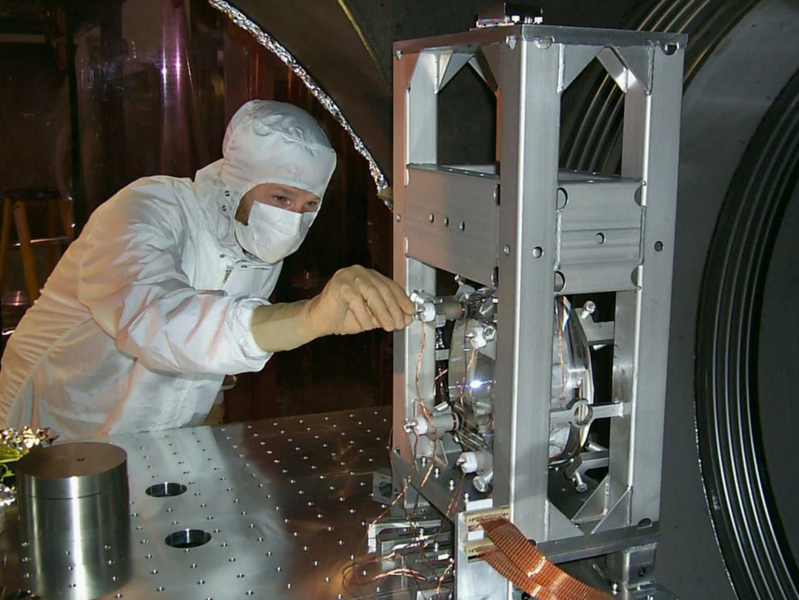 A scientist adjusts the position of sensors on an initial LIGO suspended optic. Clean-room garb is required for all work inside the vacuum chambers to control contamination on low-loss mirrors.