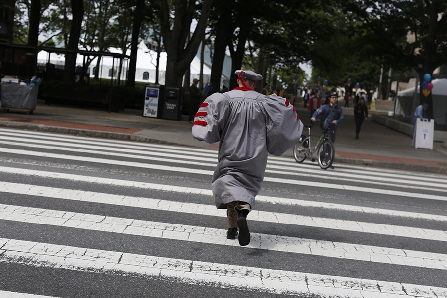 A graduating student races across Massachusetts Avenue to the hooding ceremony.