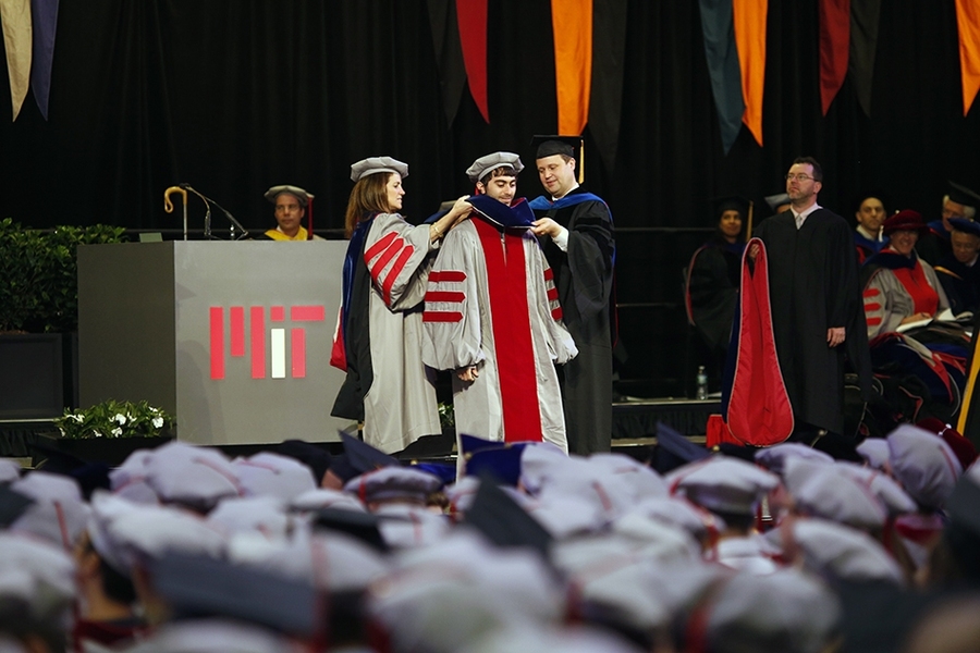 Chancellor Cynthia Barnhart (left) assists in hooding a degree candidate.