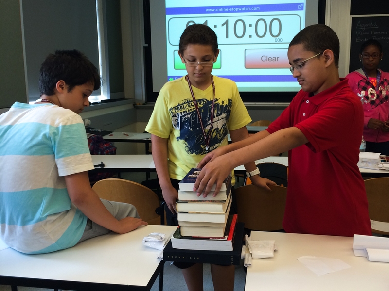 Matthew Gjanci of Boston, Medhi Kayi of Boston, and Giancarlos Jamie-Guzman of Lawrence test the strength of paper bridges they built during the civil engineering unit.