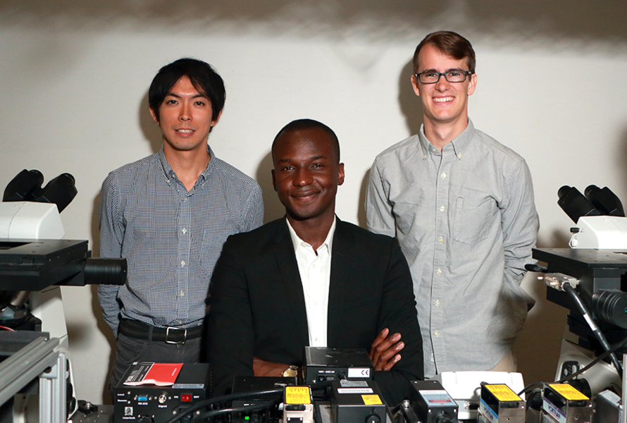 Assistant professor of physics Ibrahim Cissé (center) joins graduate students Takuma Inoue (left) and James Owen Andrews at the super-resolution microscopy setup they use to study single-molecule behavior of enzyme clusters that enable gene copying and protein production within living cells.