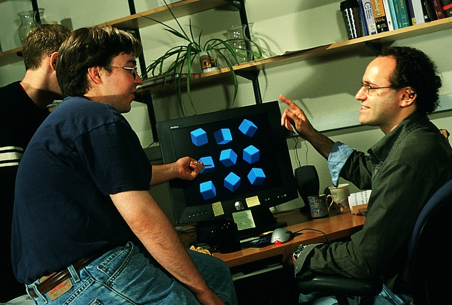 Three people speaking around computer at desk