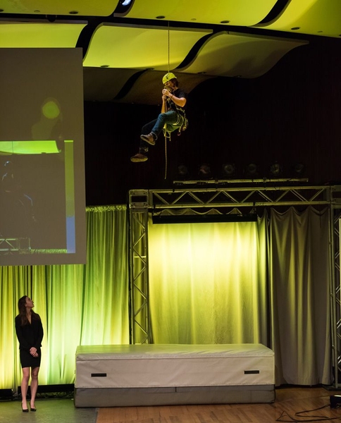 A student demonstrates a rappelling device for climbers by descending from the ceiling of Kresge.