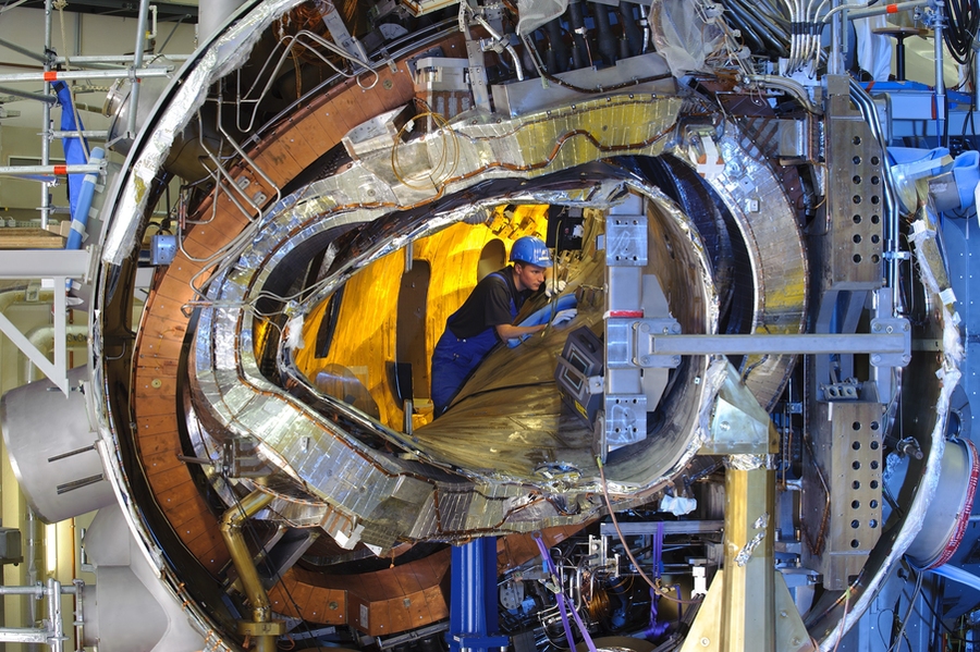 View inside one section of Wendelstein 7-X before it is completely assembled. Visible are the plasma vessel, a magnet coil, the outer casing, and numerous ducts for coolant and leads for power.