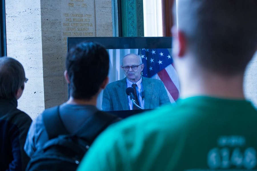 MIT community members gather in Lobby 10 to watch the NSF webcast from Washington, D. C. Onscreen is Rainer Weiss, MIT professor emeritus and a co-founder of LIGO.