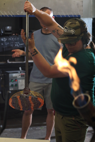 Careful lift: Jen Elek lifts a circle of fused murrini, or colored glass pieces, with a hot glass bowl at the end of a glassmaker’s tube while a torch burns in the foreground.