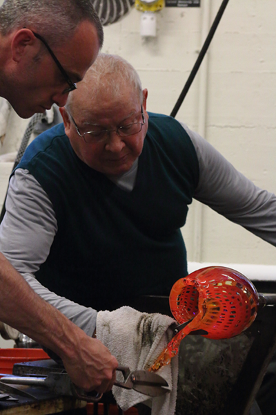 Hot trimming: Lino Tagliapietra, his hand covered with a cloth to protect against the heat, trims excess glass off a hot piece in progress, assisted by MIT Glass Lab instructor Whitney Cornforth, at left.