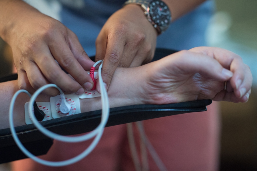 Dexter Ang presses an EMG sensor against the wrist of Bobby Forster, who is living with ALS, to measure the electrical signals that remain in his muscles.